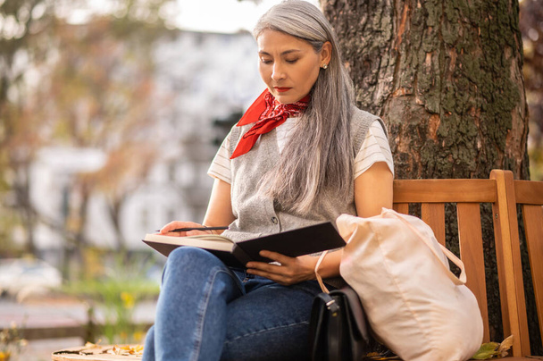 Inspiration. Woman sitting on a bench with a notebook in and looking involved - Foto, imagen