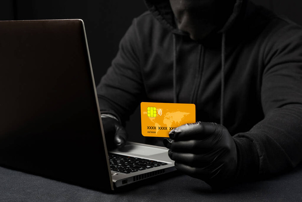 Un cibercriminal encapuchado con una tarjeta de crédito o débito. Estafas en Internet. Alerta de phishing. Acceso violado a los datos personales - Foto, Imagen