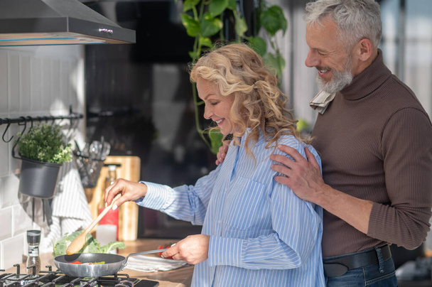 Pleaceful morning. Mature couple in the kitchen looking happy while cooking breakfast - Photo, Image