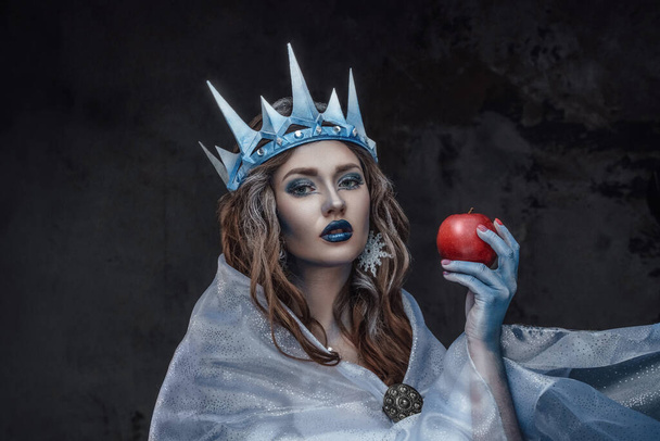 Портрет привабливої крижаної принцеси з червоним яблуком і замороженою шкірою, що дивиться на камеру
. - Фото, зображення