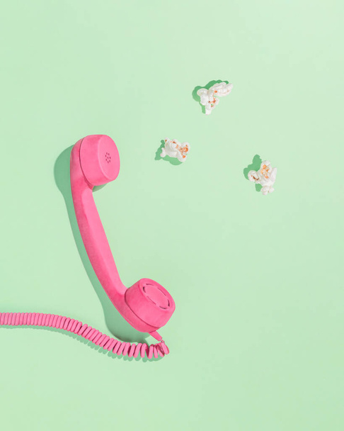 Minimale layout estetico astratto con ricevitore telefonico rosa pastello e popcorn su sfondo isolato verde pastello con ombre. Piatto. Concetto di svago. Biglietto d'invito. - Foto, immagini