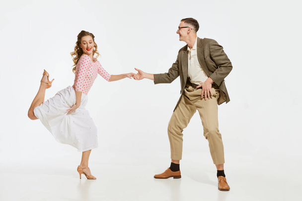 Two emotional dancers in vintage style clothes dancing swing dance, rock-and-roll isolated on white background. Timeless traditions, 1960s american fashion style and art. Couple look happy, delighted - Foto, imagen