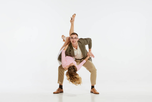 Love in motion. Young excited man and woman wearing 60s american fashion style clothes dancing retro dance isolated on white background. Music, energy, happiness, mood, action - Fotó, kép