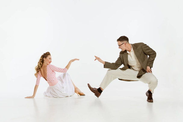 Love in motion. Young excited man and woman wearing 60s american fashion style clothes dancing retro dance isolated on white background. Music, energy, happiness, mood, action - Fotoğraf, Görsel