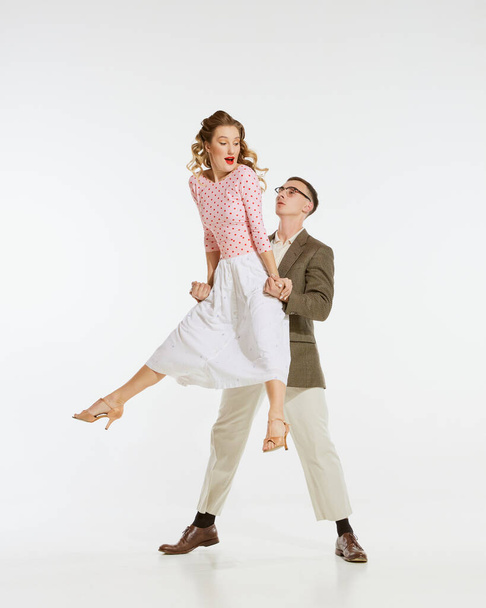 Love in motion. Young excited man and woman wearing 60s american fashion style clothes dancing retro dance isolated on white background. Music, energy, happiness, mood, action - Photo, Image