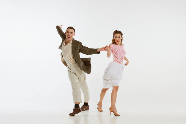 Two emotional dancers in vintage style clothes dancing swing dance, rock-and-roll isolated on white background. Timeless traditions, 1960s american fashion style and art. Couple look happy, delighted - Foto, Imagen