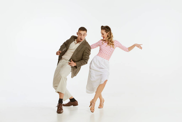 Love in motion. Young excited man and woman wearing 60s american fashion style clothes dancing retro dance isolated on white background. Music, energy, happiness, mood, action - Photo, Image