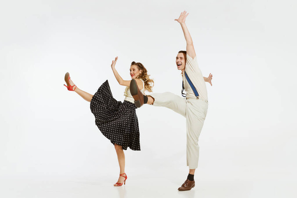 Love in motion. Young excited man and woman wearing 60s american fashion style clothes dancing retro dance isolated on white background. Music, energy, happiness, mood, action - Zdjęcie, obraz