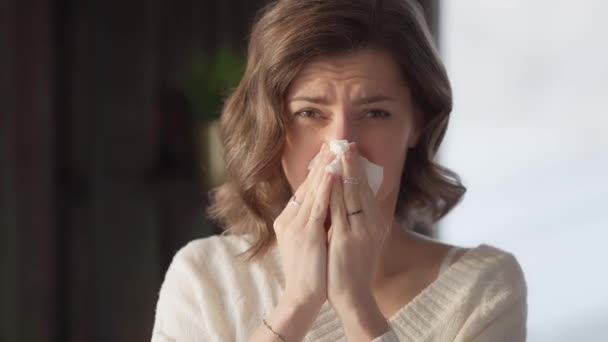 A young woman looking at the camera blows her nose into a paper napkin. Runny nose in an adult with a weakened immune system. The manifestation of a cold or allergy. - Footage, Video