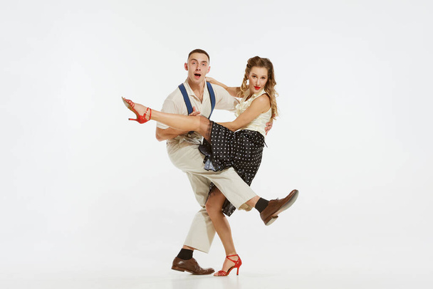 Two emotional dancers in vintage style clothes dancing swing dance, rock-and-roll isolated on white background. Timeless traditions, 1960s american fashion style and art. Couple look happy, delighted - Fotografie, Obrázek