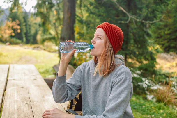 Thirsty girl drinking water in sun lights, hiking by forest. Autumn hike in forest. Adventure in nature. Active lifestyle - Photo, Image