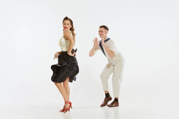 Láska v pohybu. Mladý vzrušený muž a žena na sobě 60s amerického módního stylu oblečení tanec retro tanec izolované na bílém pozadí. Hudba, energie, štěstí, nálada, akce - Fotografie, Obrázek