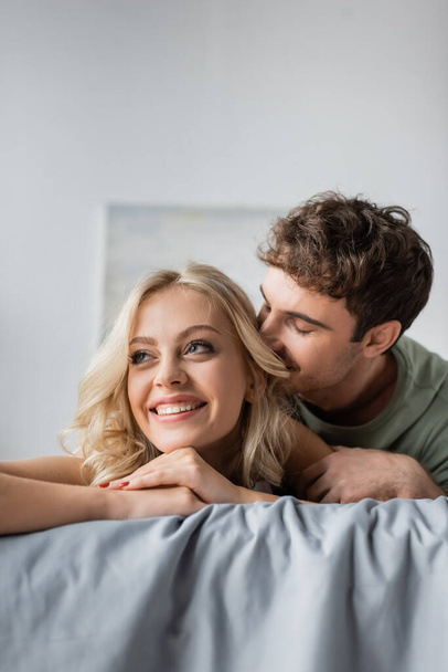 Mann im Pyjama küsst hübsche blonde Freundin auf Bett  - Foto, Bild