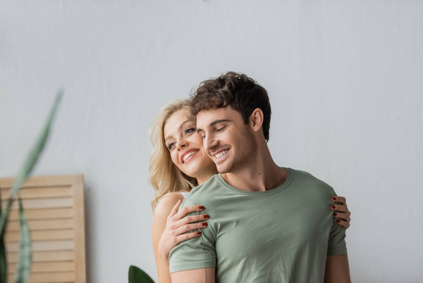 Cheerful woman hugging brunette boyfriend in pajama at home  - Photo, Image
