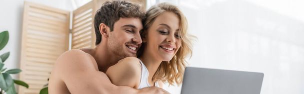 Shirtless man hugging smiling girlfriend near laptop at home, banner  - Photo, Image
