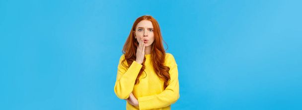 Woman gossiping with colleagues found out shocking revelation. Speechless and concerned young redhead female student heard rumour or bad news, folding lips frowning frustrated, blue background. - Foto, Imagem