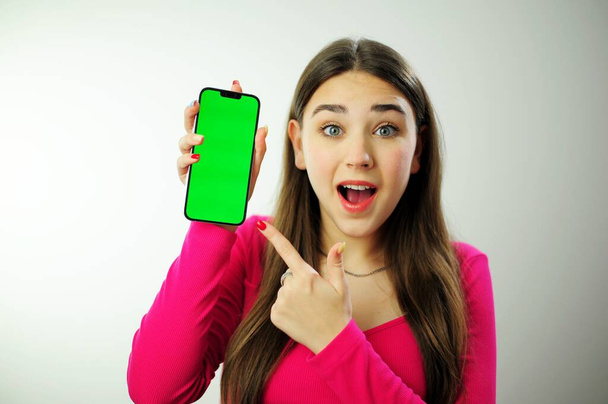 a woman in a pink sweater with multi-colored manicure long hair is happy showing her phone she has blue eyes she is happy advertising was looking for what she found girl phone chromakey delight - Fotó, kép