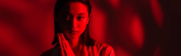 portrait of asian woman with praying hands looking at camera on dark background with red light, banner - Photo, Image