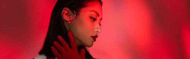 portrait of asian woman in glove and ear cuff on abstract background with red light, banner - Zdjęcie, obraz