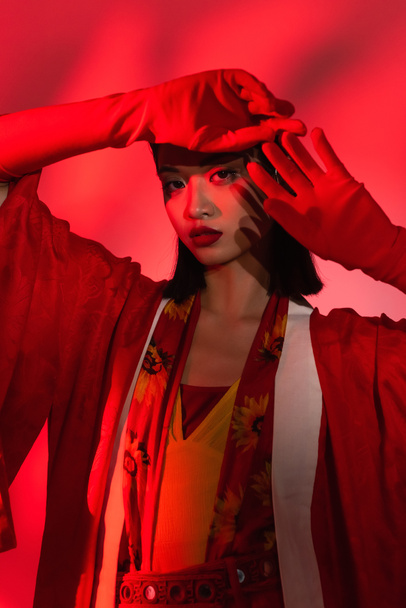 молода азіатка в елегантному кімоно мисі і рукавички позують на абстрактному фоні з червоним відтінком
 - Фото, зображення