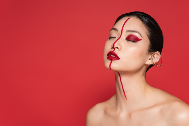 portrait of asian woman with closed eyes and artistic makeup isolated on red - Foto, Imagem