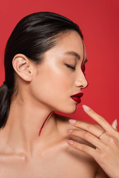 profilja ázsiai nő csukott szemmel és kreatív arccal kéz mellett arc elszigetelt on red - Fotó, kép