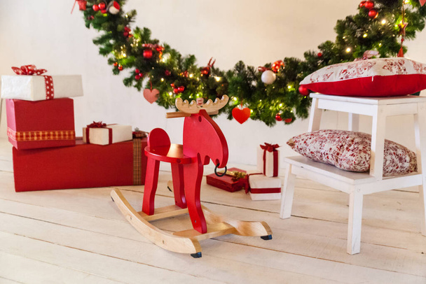 Studio or home Christmas interior with a big decorated wreath, rocking chair elk, present boxes, wooden white ladder chair with red pillows - Foto, afbeelding