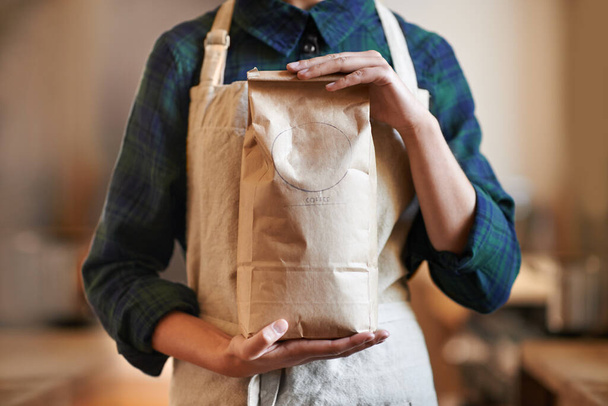 She knows how to make the best cup of coffee. a woman holding a bag while wearing an apron - Foto, Imagem
