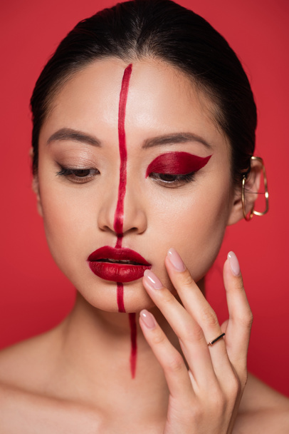 retrato de joven asiático mujer artístico maquillaje y oreja manguito tocar cara aislado en rojo - Foto, imagen
