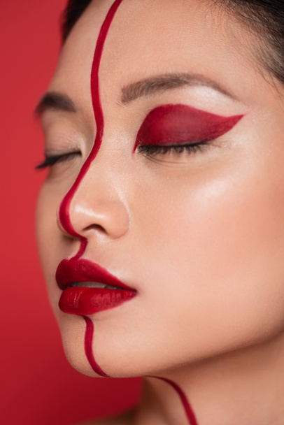 close up portrait of asian woman with closed eyes and creative visage on face divided with line isolated on red - Photo, Image