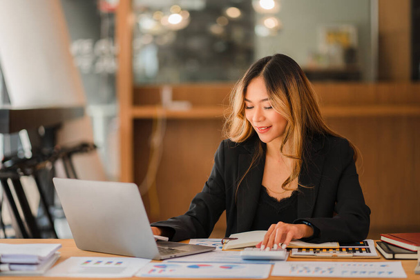 Azjatycka businesswoman z laptopem i wykresem finansowym w analizach w biurze Piękna dziewczyna z tabletem i książeczką czekową płacąca rachunki szczęśliwie rozpoczynająca koncepcję kalkulacji finansów biznesowych - Zdjęcie, obraz