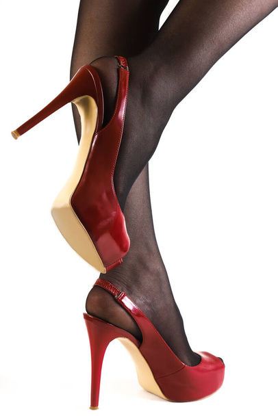 A pair of slender female legs in dark stockings with red high-heeled shoes on a white background. Close-up - Foto, Bild