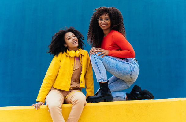 Young happy women posing on colored blue and yellow colored walls. Teenagers girl spending time together after school - Foto, Imagem