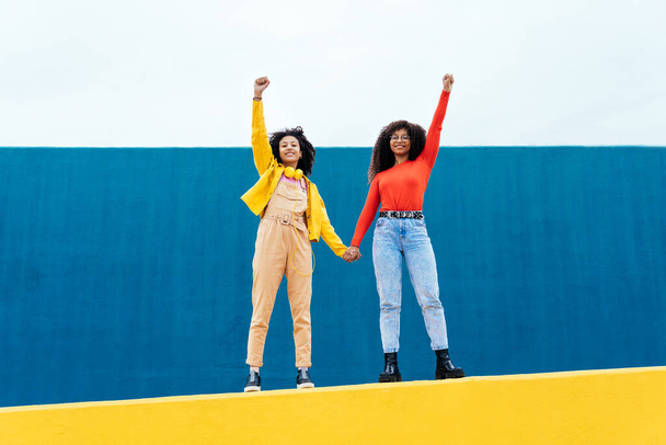 Young happy women posing on colored blue and yellow colored walls. Teenagers girl spending time together after school - Fotografie, Obrázek