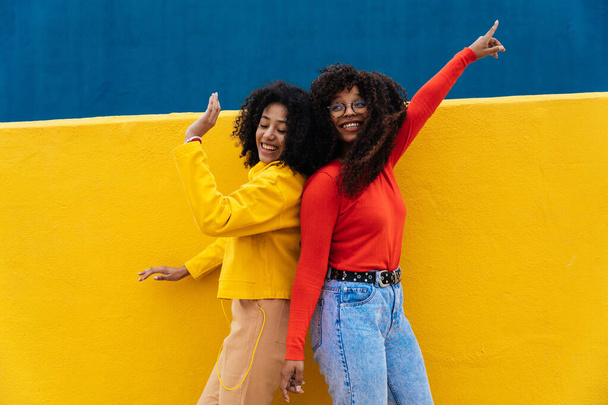 Young happy women dancing and having fun outdoor. Teenagers listening to music with smartphone and headphones in a yellow and blue modern urban area - Foto, immagini