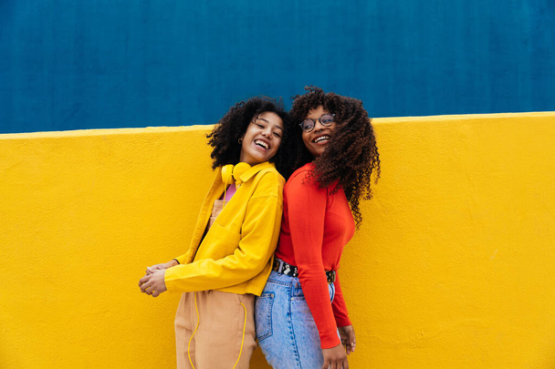 Young happy women dancing and having fun outdoor. Teenagers listening to music with smartphone and headphones in a yellow and blue modern urban area - Photo, image