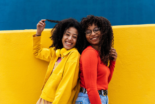 Young happy women dancing and having fun outdoor. Teenagers listening to music with smartphone and headphones in a yellow and blue modern urban area - Foto, afbeelding