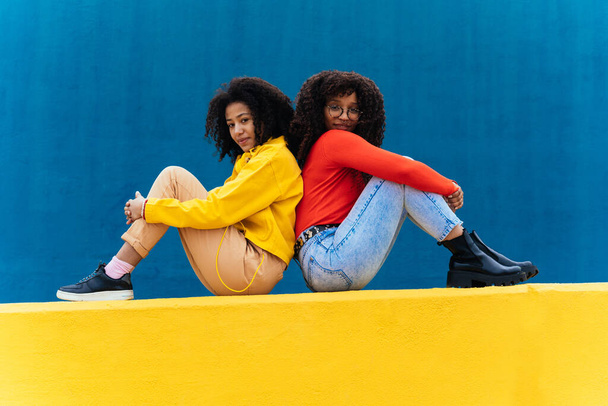 Young happy women posing on colored blue and yellow colored walls. Teenagers girl spending time together after school - Foto, Imagen