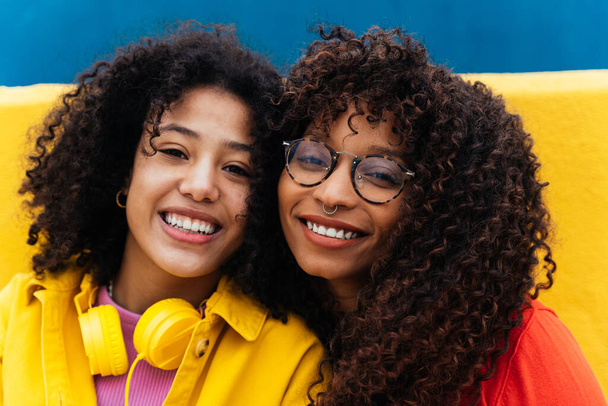 Fiatal boldog nők táncolnak és szórakoznak a szabadban. Tinédzserek zenét hallgatni okostelefonnal és fejhallgatóval egy sárga és kék modern városi területen - Fotó, kép