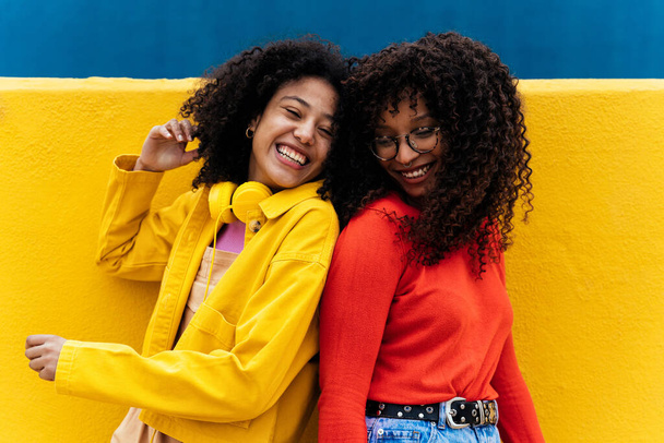 Young happy women dancing and having fun outdoor. Teenagers listening to music with smartphone and headphones in a yellow and blue modern urban area - Foto, imagen