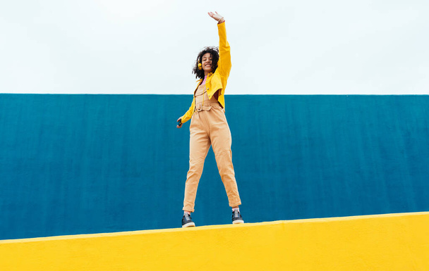 Young happy woman dancing and having fun outdoor. Teenager listening to music with smartphone and headphones in a yellow and blue modern urban area - Foto, Imagem