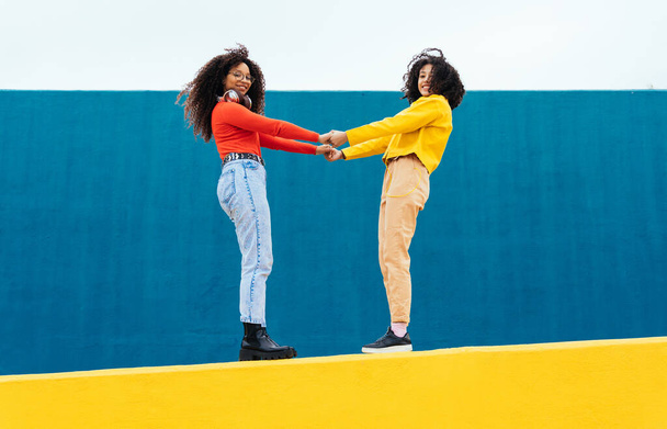 Young happy women dancing and having fun outdoor. Teenagers listening to music with smartphone and headphones in a yellow and blue modern urban area - Foto, Imagen
