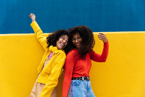 Young happy women dancing and having fun outdoor. Teenagers listening to music with smartphone and headphones in a yellow and blue modern urban area - Photo, Image
