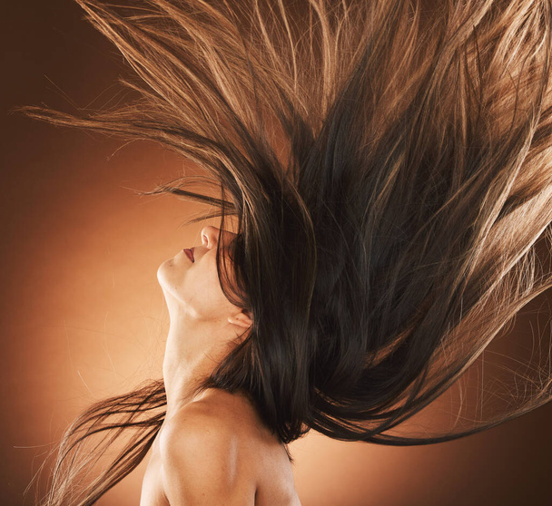 Beauty, hair and freedom with a model woman in studio on a brown background for strong haircare. Wellness, luxury and salon with an attractive young female hair flick to promote a keratin product. - Фото, изображение