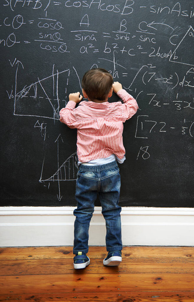 Uitdaging geaccepteerd. een jonge jongen met een schoolbord vol wiskundige vergelijkingen - Foto, afbeelding