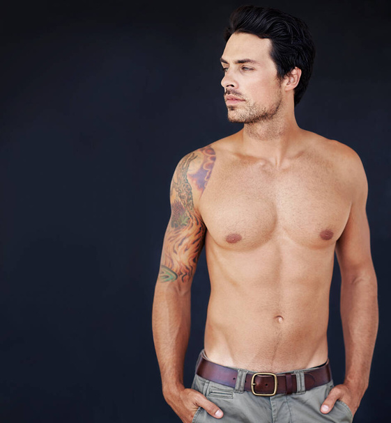 His tattoo brings an edge to his boyish good looks. handsome male with his shirt off with a dark background - Photo, Image