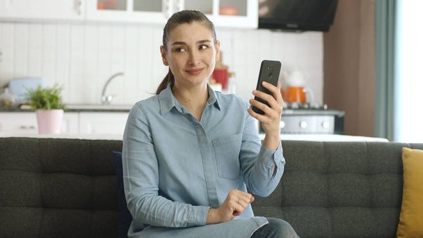Jeune femme lisant des nouvelles ou du texte au téléphone à la maison. Femme surfant sur Internet, surfant sur les comptes de médias sociaux, regardant l'espace publicitaire vide à gauche de la caméra. - Photo, image