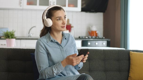 Happy woman dancing to music with headphones connected to her mobile phone in her peaceful home.Woman looking at empty advertising space to the right of the camera listening to music with wireless headphones. - Zdjęcie, obraz