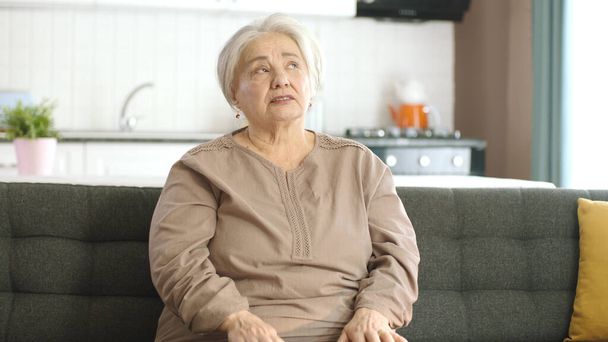 Huzurlu yaşlı kadın sessiz evinde kanepede dinleniyor. Yalnız, beyaz saçlı kadın kameranın sağındaki boş reklam alanına konuşuyor. Yaratıcı insanlar istedikleri yere istediklerini koyabilirler.  - Fotoğraf, Görsel