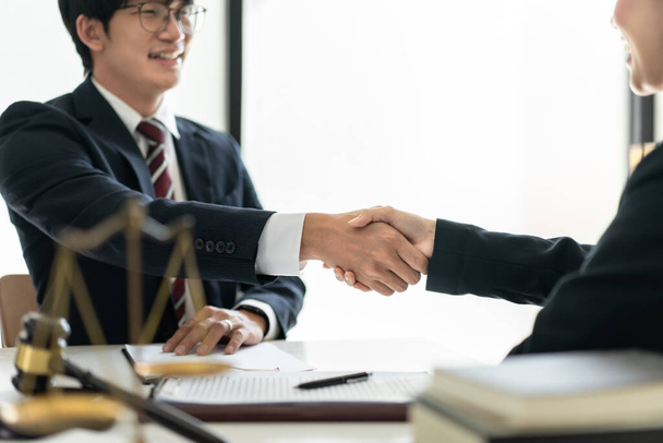 Female lawyer shaking hands with client after discussing deal of agreement together and signing contract on the table with brass scales and justice hammer in law firm. - Photo, Image
